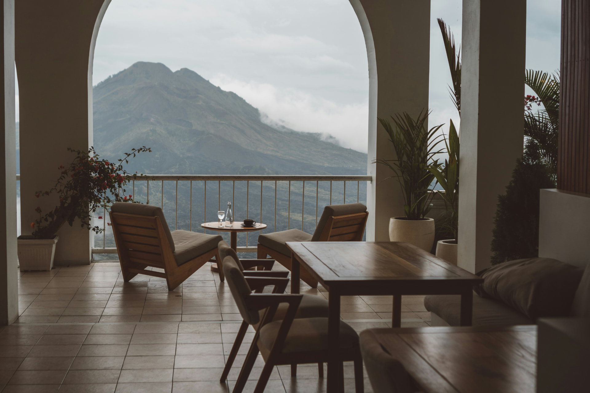Terrace beneath white arches with timber lounge chairs facing a mountain in the clouds