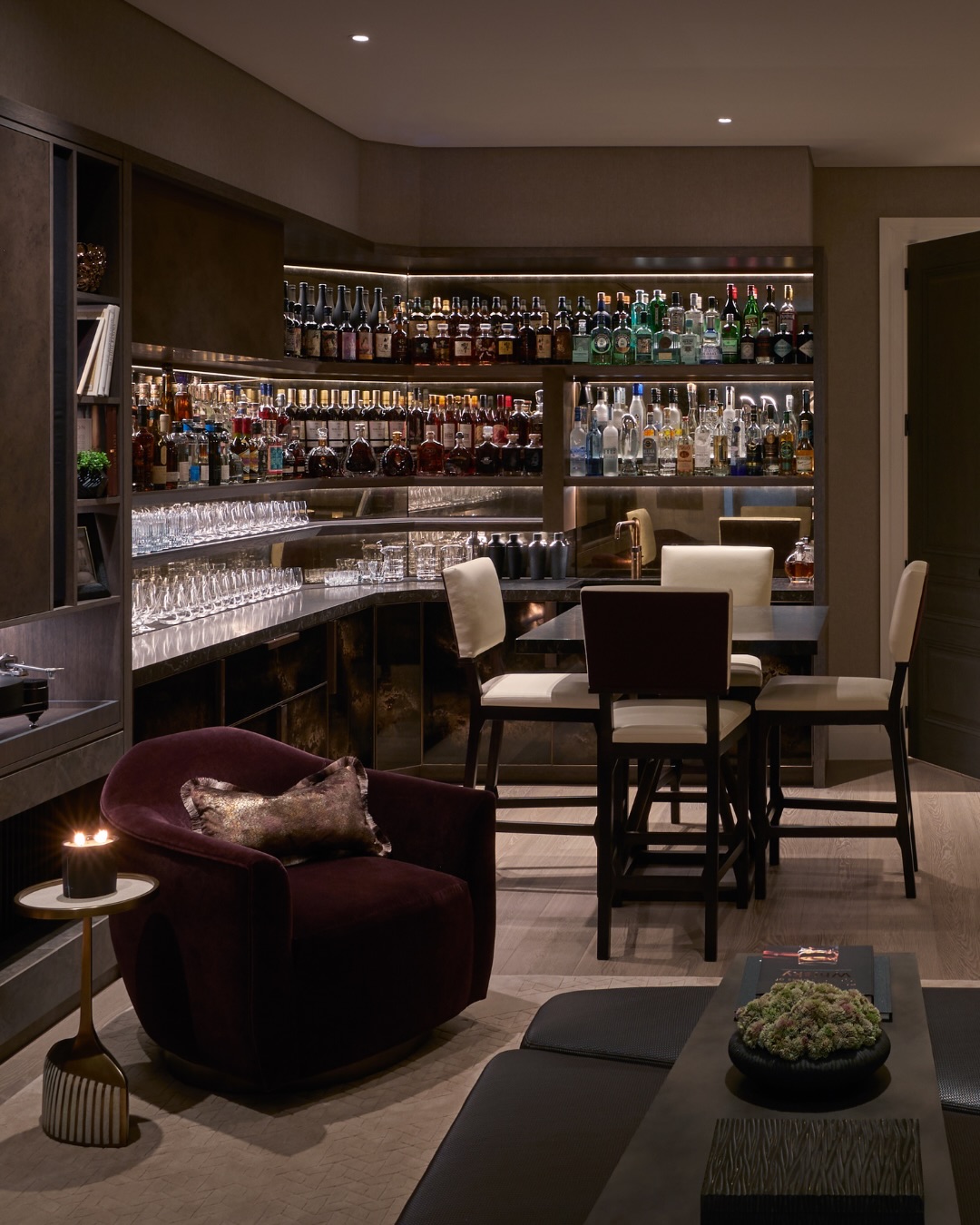 Private bar with warm lighting, backlit shelves and a velvet armchair
